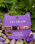 Cat collar with colorful design on a purple card labeled 'Wassily Catdinsky' against a natural background.