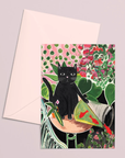 Greeting card with a black cat illustration on a floral background, accompanied by a matching envelope.