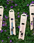 Five Fuzzyard cat collars in packaging on a green leafy background with purple flowers