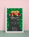 A framed art print featuring a stylized representation of Frida Kahlo as a cat, with flowers on its head and the name 'Frida Catlo' written at the bottom, set against a green background.