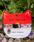 Cat collar with colorful pattern on a red and white card labeled 'Cat Collar' by Andy Pawhol, set against a natural background.