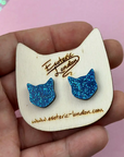 Blue glitter cat-shaped earrings on a wooden card with 'Esoteric London' branding.