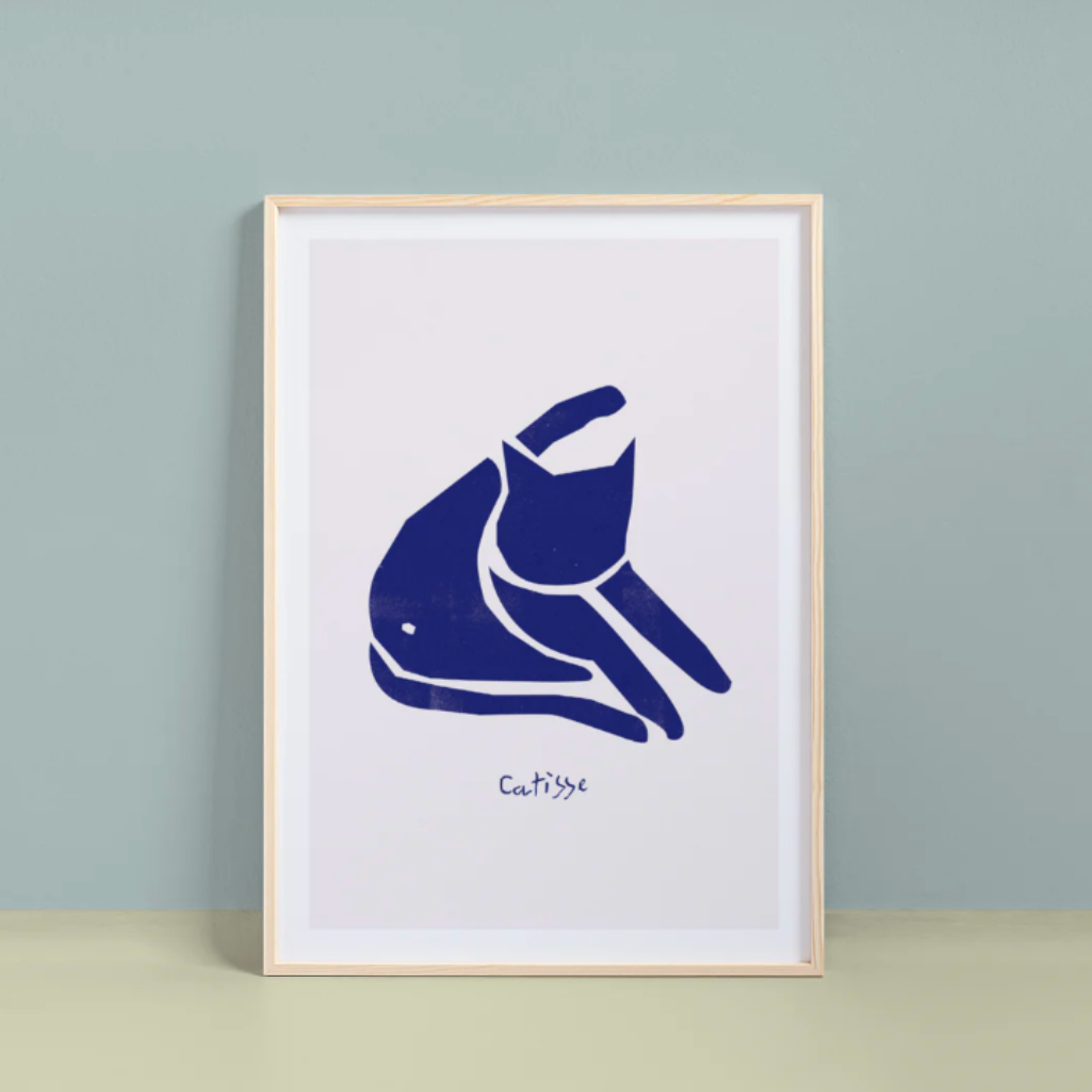 Framed artwork of a blue cat illustration on a white background, leaning against a light gray wall.