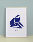 Framed artwork of a blue cat illustration on a white background, leaning against a light gray wall.
