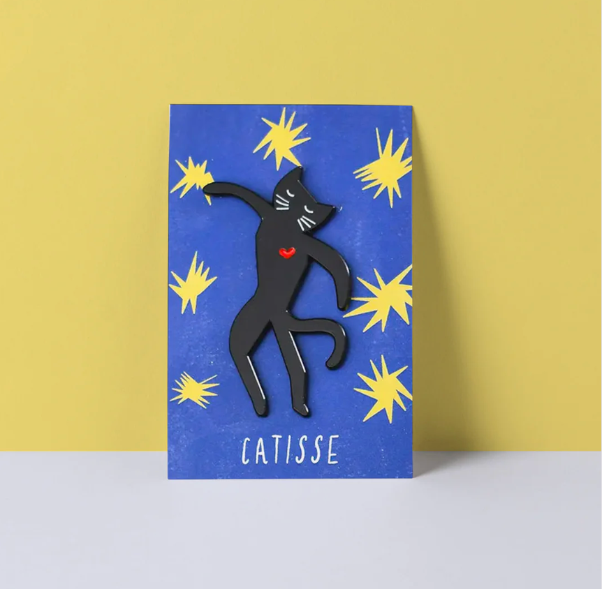 Black cat brooch on a blue card with yellow star patterns and &#39;CATISSE&#39; branding.