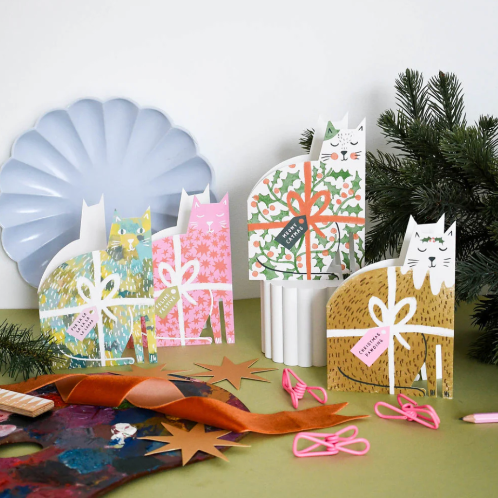 Decorative gift cards with festive cat designs on a table with Christmas decorations.