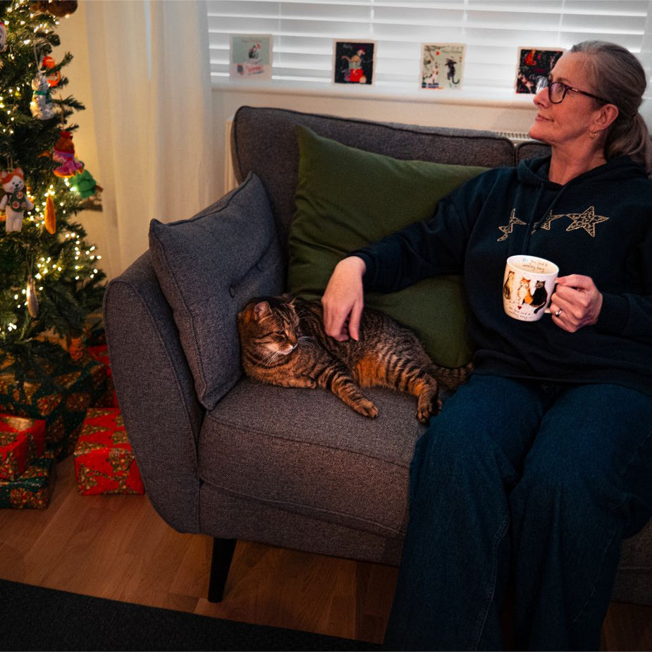 cat sitter sitting with a cat on a couch with a christmas tree and presents in the background