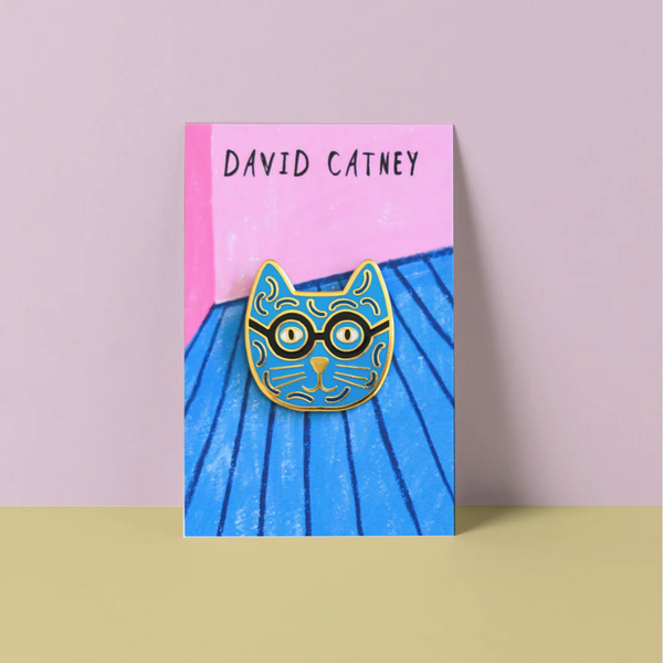 Cat-shaped pin with glasses on a blue and pink card by David Catney
