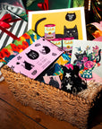 Basket of cat-themed greeting cards with colorful designs on a wooden surface.
