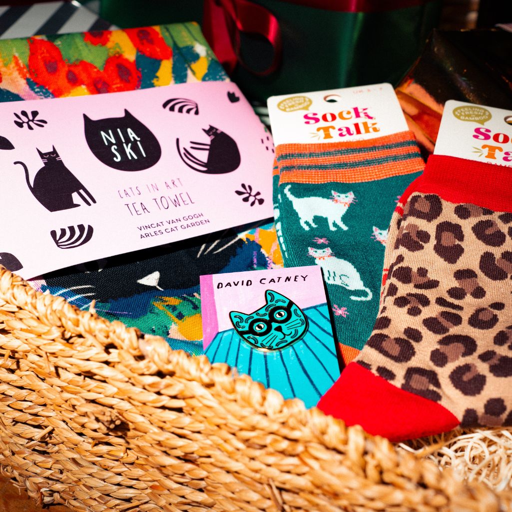 Cat-themed products including socks, tea towels, and cards in a basket.