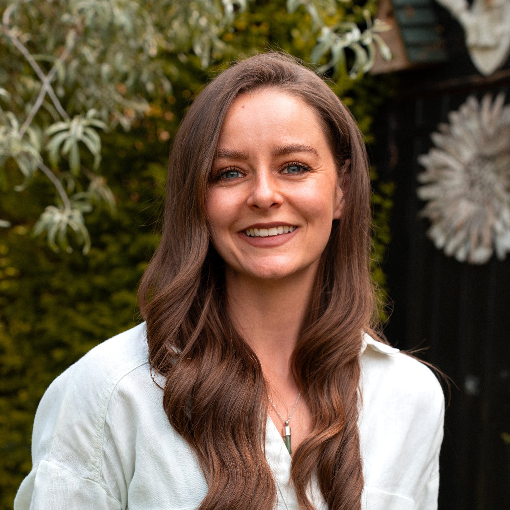 Woman with long brown hair wearing a light-colored shirt outdoors.