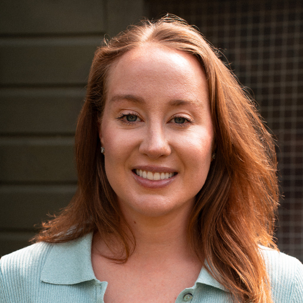 Woman with red hair wearing a light blue shirt against a neutral background
