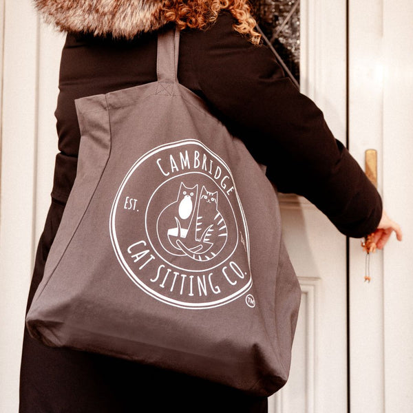 Person holding a tote bag with 'Cambridge Cat Sitting Co.' logo.