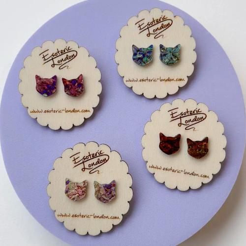 Cat-shaped earrings on 'Exotic London' branded cards against a purple background