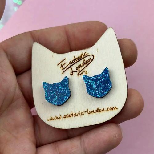 Blue glitter cat-shaped earrings on a wooden card with &#39;Esoteric London&#39; branding.