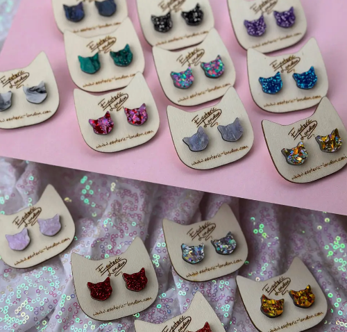 Cat-shaped earrings on display with a pink and glittery background