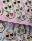 Cat-shaped earrings on display with a pink and glittery background