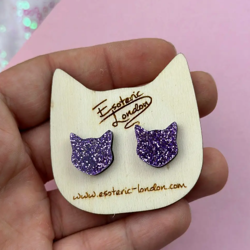 Purple glitter cat-shaped earrings on a wooden card with &#39;Esoteric London&#39; branding.