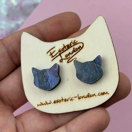 Cat-shaped earrings on a wooden display card held by a hand with &#39;Esoteric London&#39; branding.