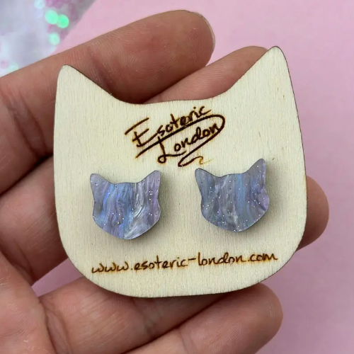 Cat-shaped wooden display card with blue cat-shaped earrings held by a hand against a pink background.